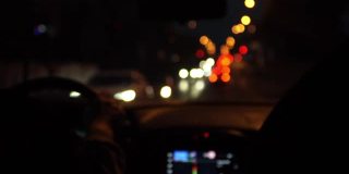 在大夜间城市的道路从驾驶汽车内的观点。从正面窗口看到的模糊的汽车前灯。