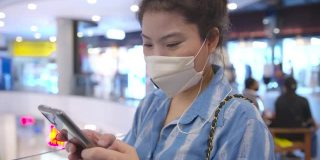 迷人的亚洲女性休闲服戴口罩防毒手用智能手机数码设备在商场超市背景