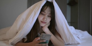年轻的亚洲女子享受在床上使用智能手机的场景