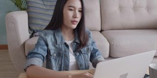 一位美丽的年轻亚洲女子正在家中用电脑和她的同事通过技术进行视频会议