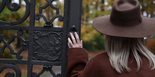 穿着棕色外套的时尚女孩在秋天公园附近的大门