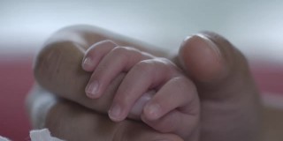当她的宝宝在温柔和爱中睡觉的时候，靠近妈妈抚摸新生婴儿的手。幸福的家庭的概念。