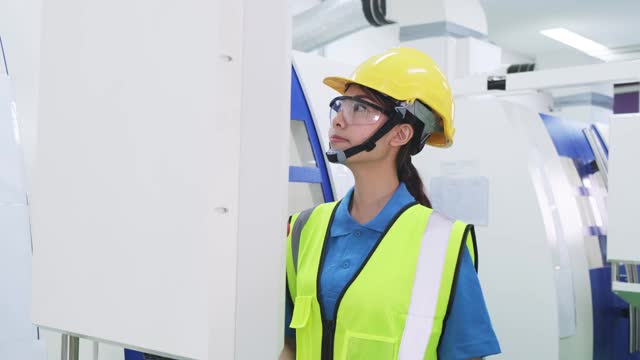 工厂生产线上戴防护安全帽和眼镜的女工。在工业工厂的高科技机器上操作的女孩有自信和微笑的脸。