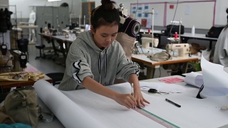 亚洲华裔女时装大学生在学院车间做服装项目，写下尺寸，画出缝纫图案视频素材模板下载