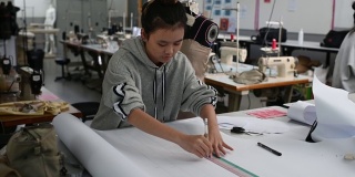亚洲华裔女时装大学生在学院车间做服装项目，写下尺寸，画出缝纫图案