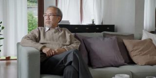 亚洲老年人老年男性或抑郁的爷爷在养老院的起居室对隔离看窗外，感觉悲伤思念不快乐周到的心理保健老年人。