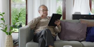 亚洲退休老人用平板电脑在线转账或金融支付，阅读文字，微笑或大笑，快乐和积极。资深亚洲人，具有数字技术理念