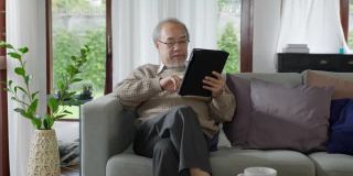 老的亚洲祖父母在家里用电脑平板电脑和孙子们一起玩和看，以增进家庭关系。年轻女孩从背后拥抱年长的男人。