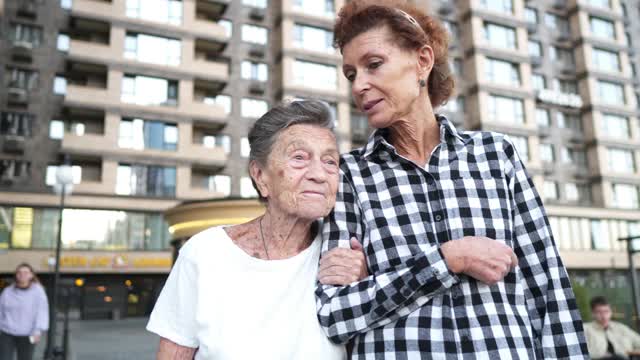 照顾老人的护士。志愿护士拥抱老年妇女，微笑，开心，走在院子里。公寓、养老院、帮助老人的概念。成熟的女儿去看望奶奶。
