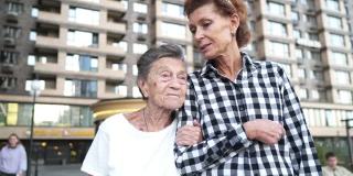 照顾老人的护士。志愿护士拥抱老年妇女，微笑，开心，走在院子里。公寓、养老院、帮助老人的概念。成熟的女儿去看望奶奶。