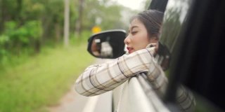 慢动作的快乐年轻美丽的亚洲女人旅行者坐在汽车与拉她的脸和手在雨天的车窗。漂亮女孩喜欢和享受户外生活方式和假期的乐趣。