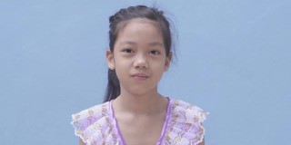 微笑自信的亚洲小女孩脸上的微笑，亚洲孩子站在蓝色的背景。一个看着相机的孩子的肖像