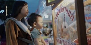 年轻的母亲和她的儿子在泰国的街头小吃市场买面条