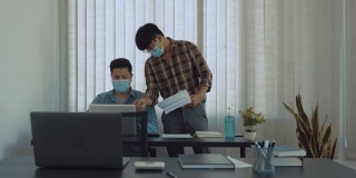 两名亚洲男子在办公室工作，戴着口罩分析企业数据。