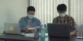 疫情期间，两名亚洲男子戴着口罩在办公室工作，分析企业数据。