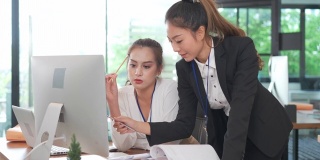 亚洲女商人经理在现代商务办公桌上用电脑与年轻的女同事或新员工讨论信息。