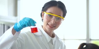 迷人的女科学家们戴着护目镜和手套，在一个科学化学实验室的试管中测试这种红色液体。