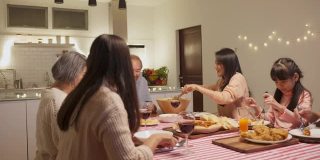 幸福的家庭时间和关系，亚洲大家庭有一个小聚会，一起在家里吃东西。爷爷很高兴看到他的孩子和侄子在家里的餐桌上吃饭，分享食物。