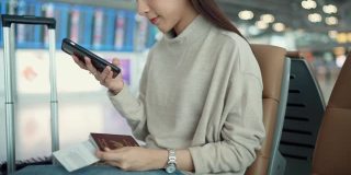年轻的亚洲游客坐在空空如也的候机大厅里浏览智能手机。