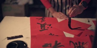 亚洲华人女性练习书法的手，为即将到来的中国新年庆祝家庭装饰目的与繁荣和良好的措词写在一张红色的纸上