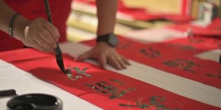 亚洲华人男性练习书法的手，为即将到来的中国新年庆祝家庭装饰目的繁荣和良好的措词写在一张红色的纸上