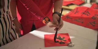 一位亚洲华人父亲在练习中国新年的书法，并在一张红纸上教他的女儿，握着她的手