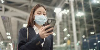 女投资者戴着医用口罩在机场用智能手机检查登机牌