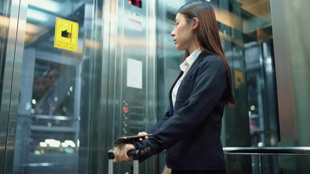 年轻的女秘书穿着正装在机场的电梯里使用智能手机