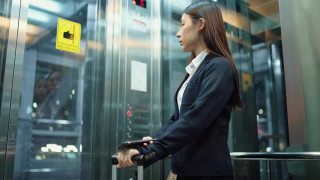 年轻的女秘书穿着正装在机场的电梯里使用智能手机视频素材模板下载