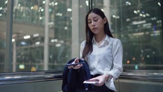 年轻的女秘书穿着正装在机场的电梯里使用智能手机视频素材模板下载