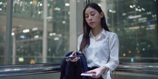 年轻的女秘书穿着正装在机场的电梯里使用智能手机