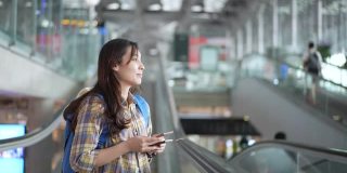 亚洲女游客在机场的自动扶梯上使用手机