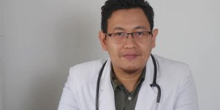 亚洲男医生对着镜头微笑，在视频通话中给出建议。在线医生远程医疗远程保健概念