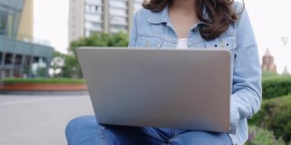 快乐的年轻亚洲女性使用笔记本电脑和耳机教育或在城市公园工作。使用免费Wi-Fi上网在户外开会或学习。概念技术视频会议