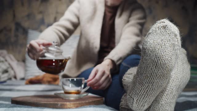 成熟的女人正坐在沙发上喝茶。注重脚上穿的羊毛手工袜子