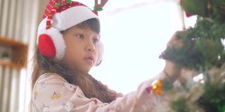 小女孩在圣诞节用装饰品装饰圣诞树