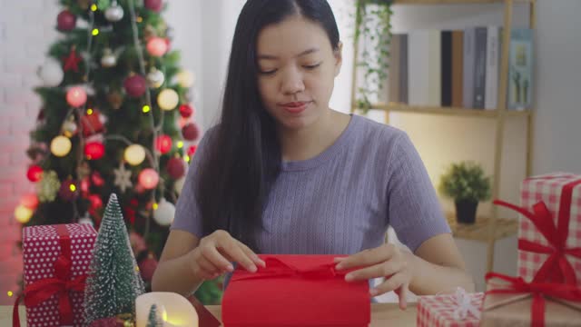 亚洲妇女打开礼盒与笑脸在家里的背景与圣诞树装饰节日节日。圣诞节庆祝活动的概念。4 k慢动作。