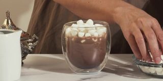女子在一杯热巧克力饮料中加入棉花糖，特写视频，大理石背景