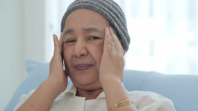 一位戴着头巾的患癌症的老妇人躺在医院的病床上，她感到头痛。