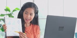 亚洲妇女在视频会议上谈论销售报告。亚洲女性使用笔记本电脑进行在线视频会议，在家办公