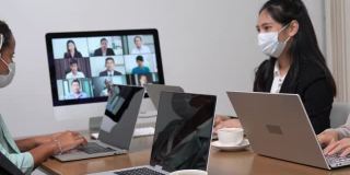 年轻的亚洲员工和员工团队通过电脑进行Zoom视频电话会议，商务人士共用办公桌使用电脑共同工作，