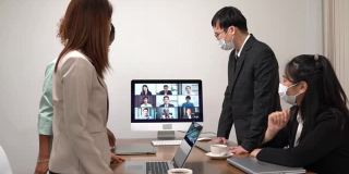 年轻的亚洲员工和资深的办公室员工团队通过电脑进行Zoom视频电话会议，商务人士共用办公桌使用电脑共同工作