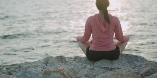 运动亚洲女性坐在冥想姿势姿势医学瑜伽调息平衡在美丽的海滩景色在日出。