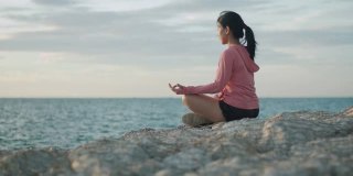 亚洲运动女性沉思坐在海边的石头日落。