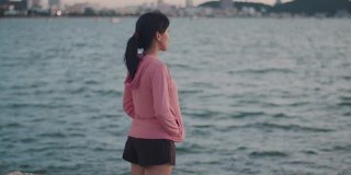 一位美丽的亚洲女跑步者站在沙滩上看海景。