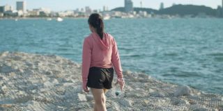 健身女性拿着水瓶在海边的岩石上行走，一边跑步一边休息，健康的生活方式运动理念。