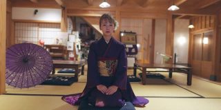 穿着Furisode和服的年轻女子坐在高跟鞋上，在日本的榻榻米房间鞠躬