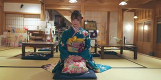穿着Furisode和服的年轻女子坐在高跟鞋上，在日本的榻榻米房间鞠躬