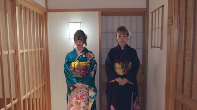 两个穿着Furisode和服的年轻女子一起走在日本旅馆的走廊上
