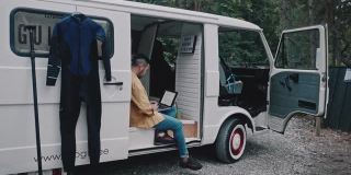 一名日本冲浪者在他的迷你面包车里的公路旅行中用笔记本电脑工作